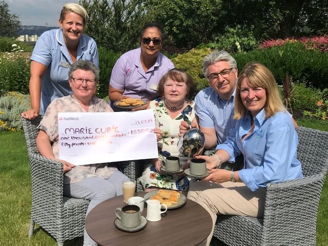 Staff and patients with Paul and Lucy at the hospice  holding a large cheque showing fundraising amount of £1,850